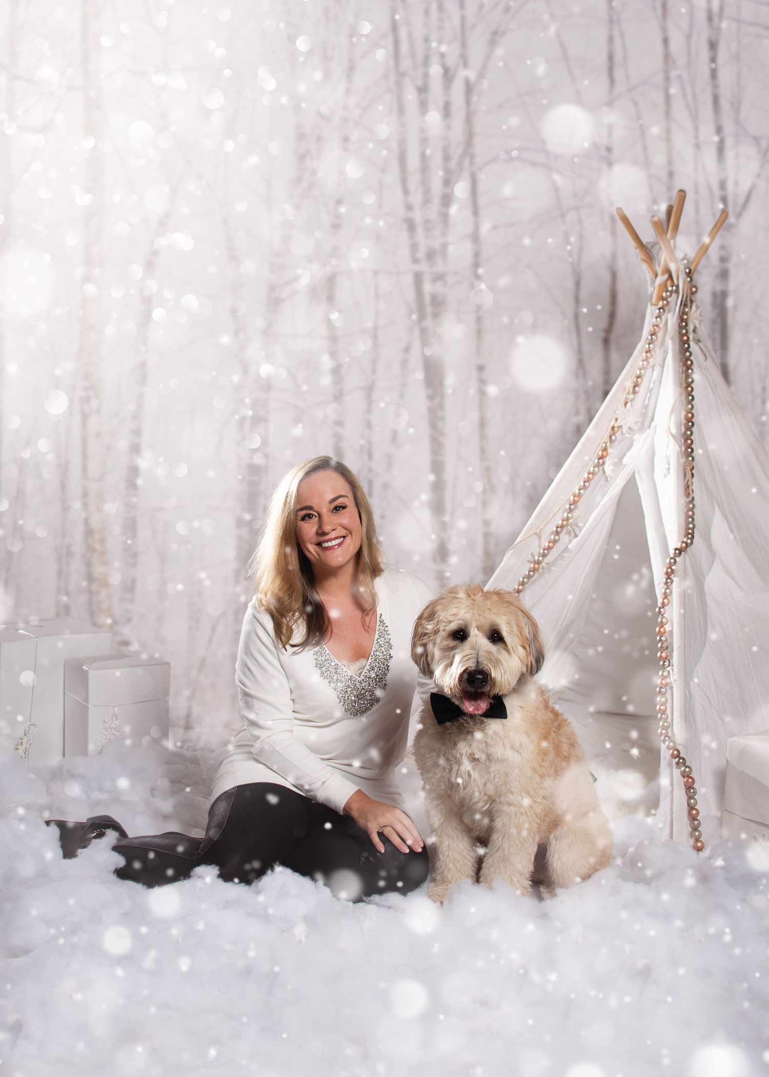A winter photography session with dogs in a snowy white forest setting with decorative lights and teepee.