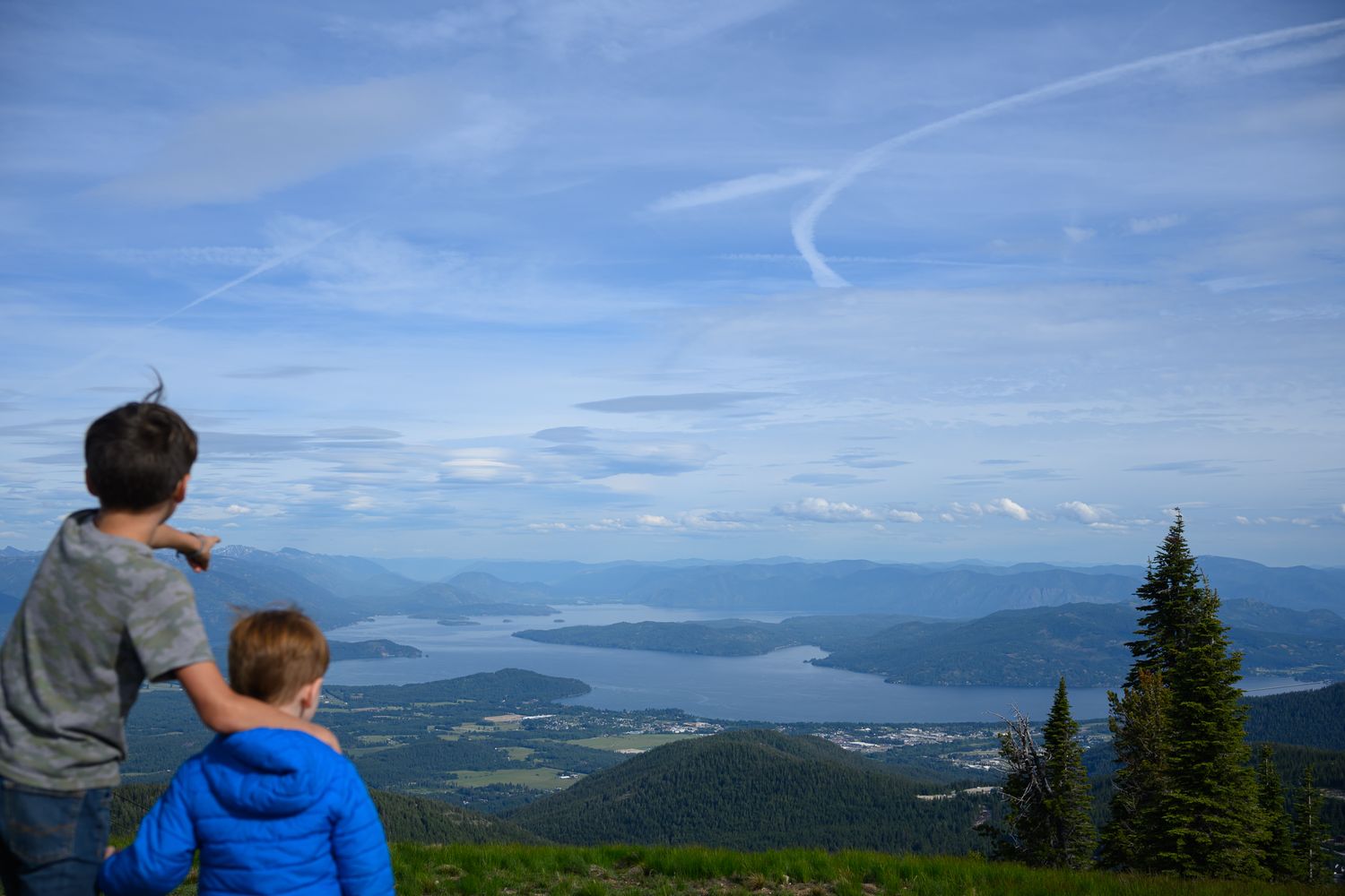 Two people admiring the panoramic view of lakes and mountains from a scenic overlook.