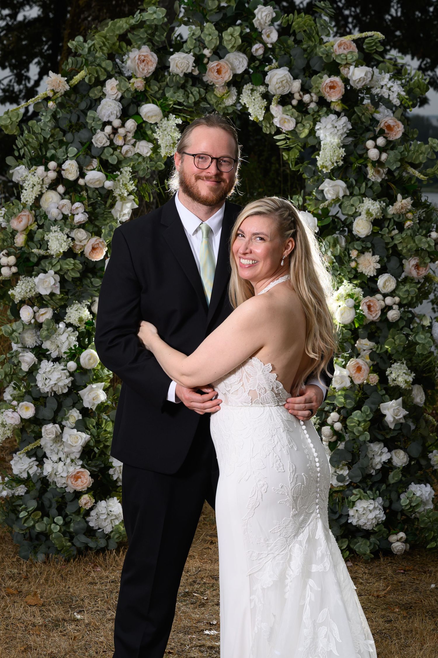 A happy couple shares a joyful moment together in front of a beautiful wall of white and pink roses.
