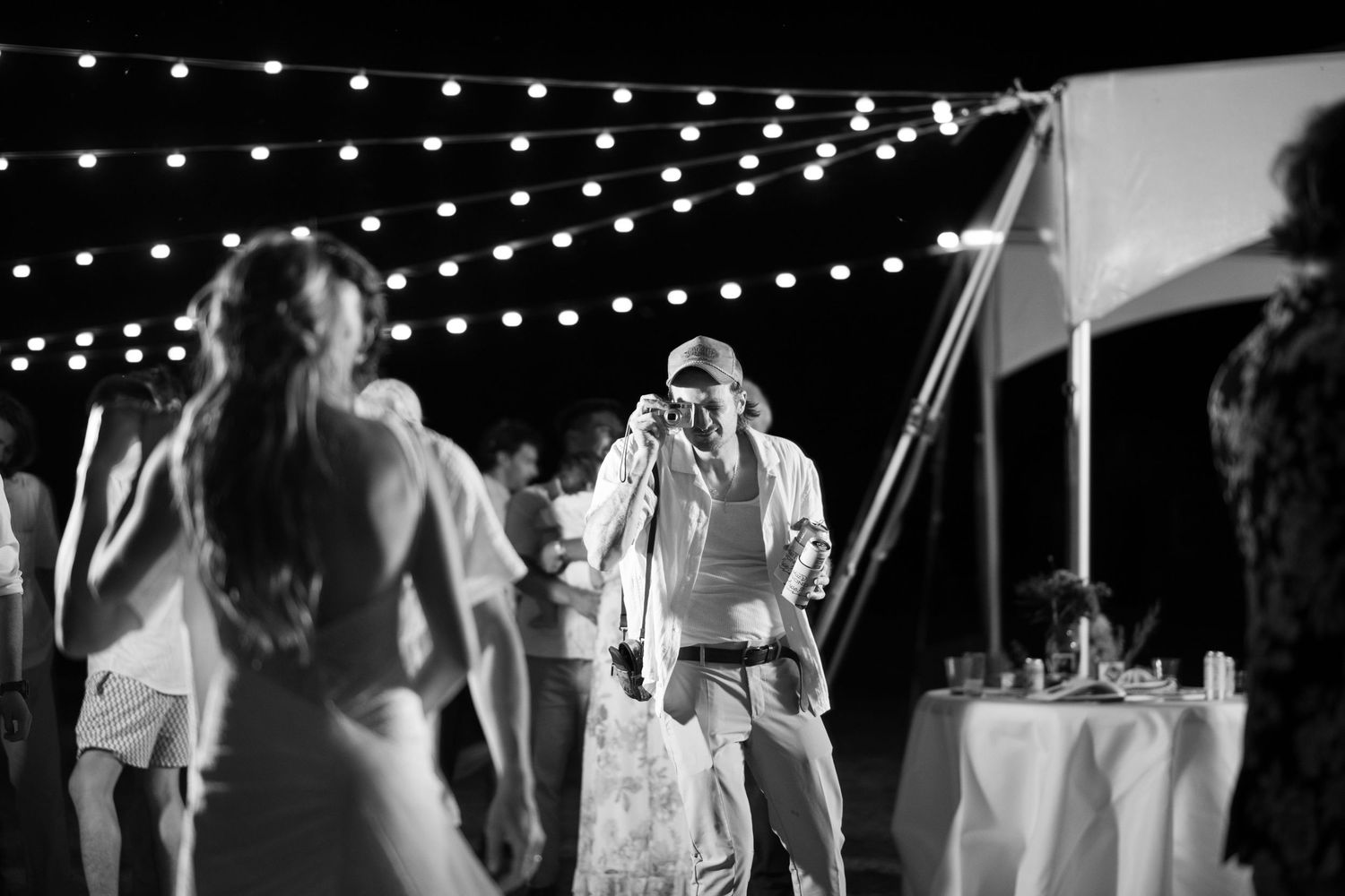 Black and white photo of string lights illuminating an outdoor evening celebration.