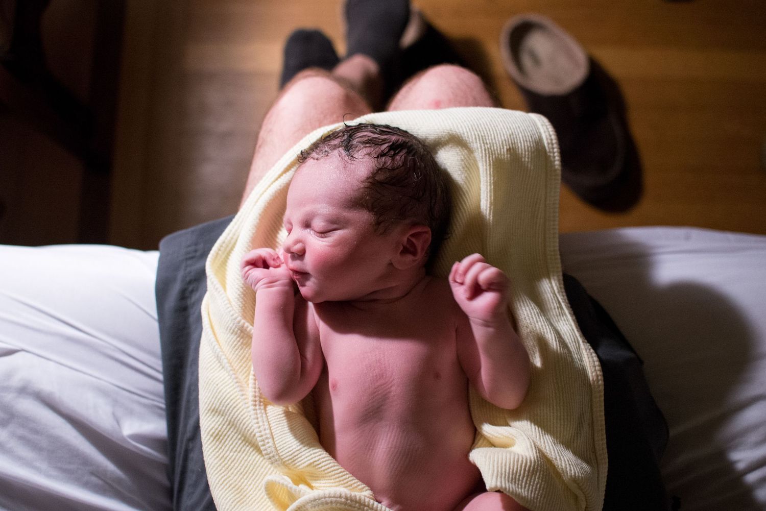 A newborn baby sleeping peacefully in a soft yellow blanket on a bed.