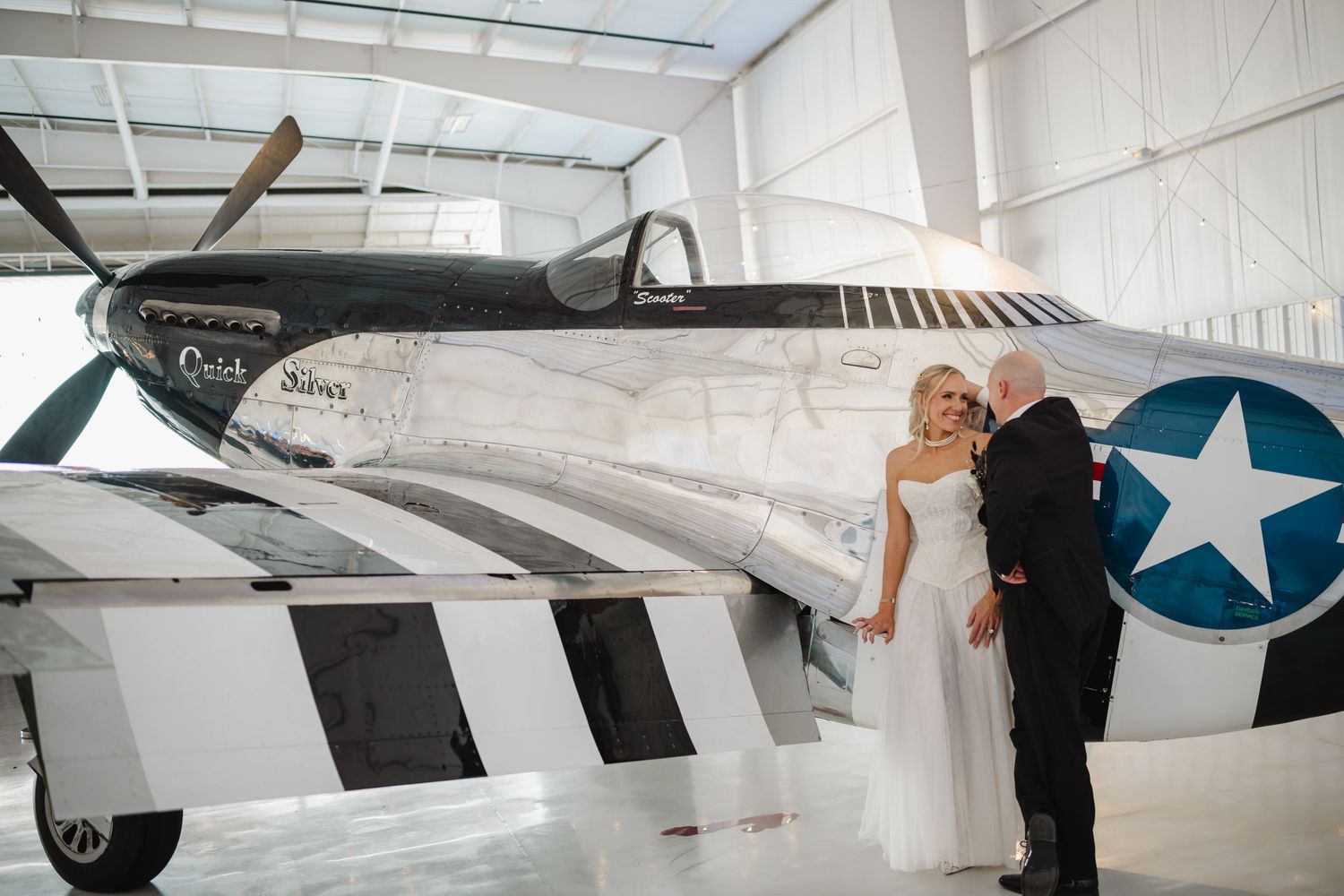 Wedding couple poses romantically beside a vintage WWII aircraft in an aviation museum hangar.