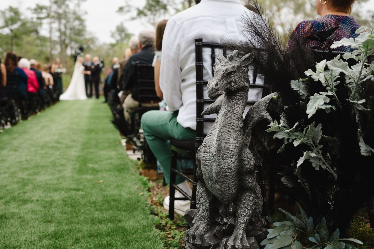 Dragon statue decoration adorns chair at outdoor wedding ceremony aisle with lush greenery.