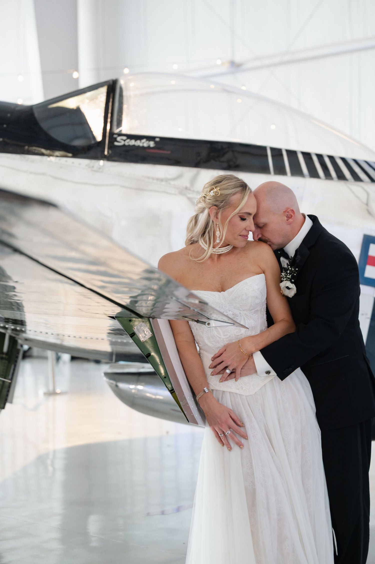 Bride and groom share a romantic embrace in front of a vintage aircraft in a wedding hangar venue.