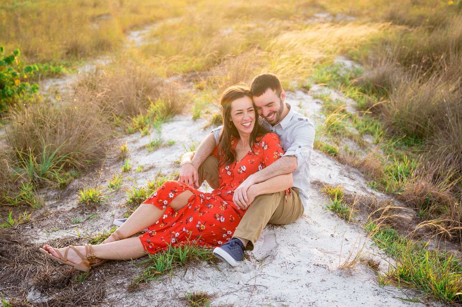 A couple in matching outfits laying together on a sandy beach path during golden hour.