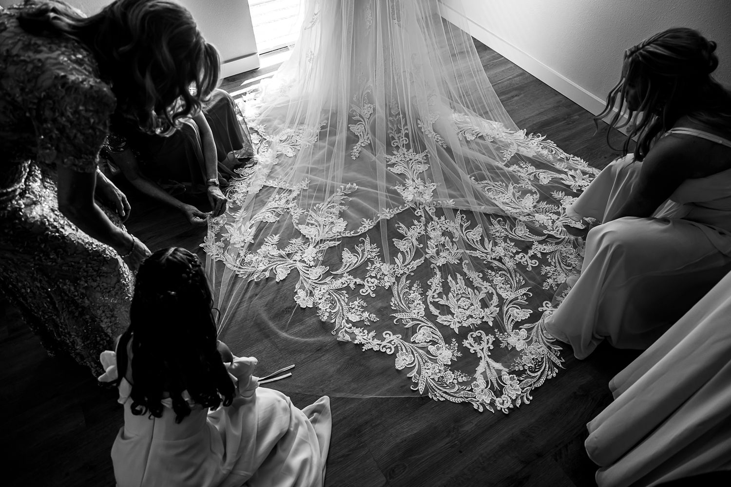 A detailed wedding dress veil with intricate lace patterns is laid out on the floor during preparation.