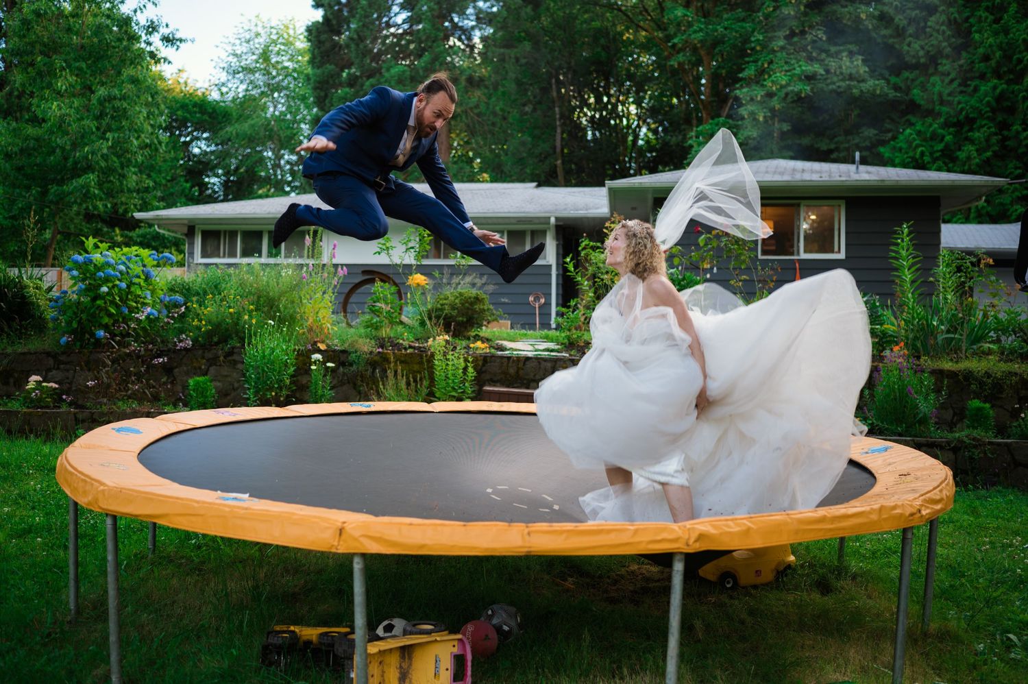 Bride bouncing on a trampoline in her wedding dress surrounded by greenery.