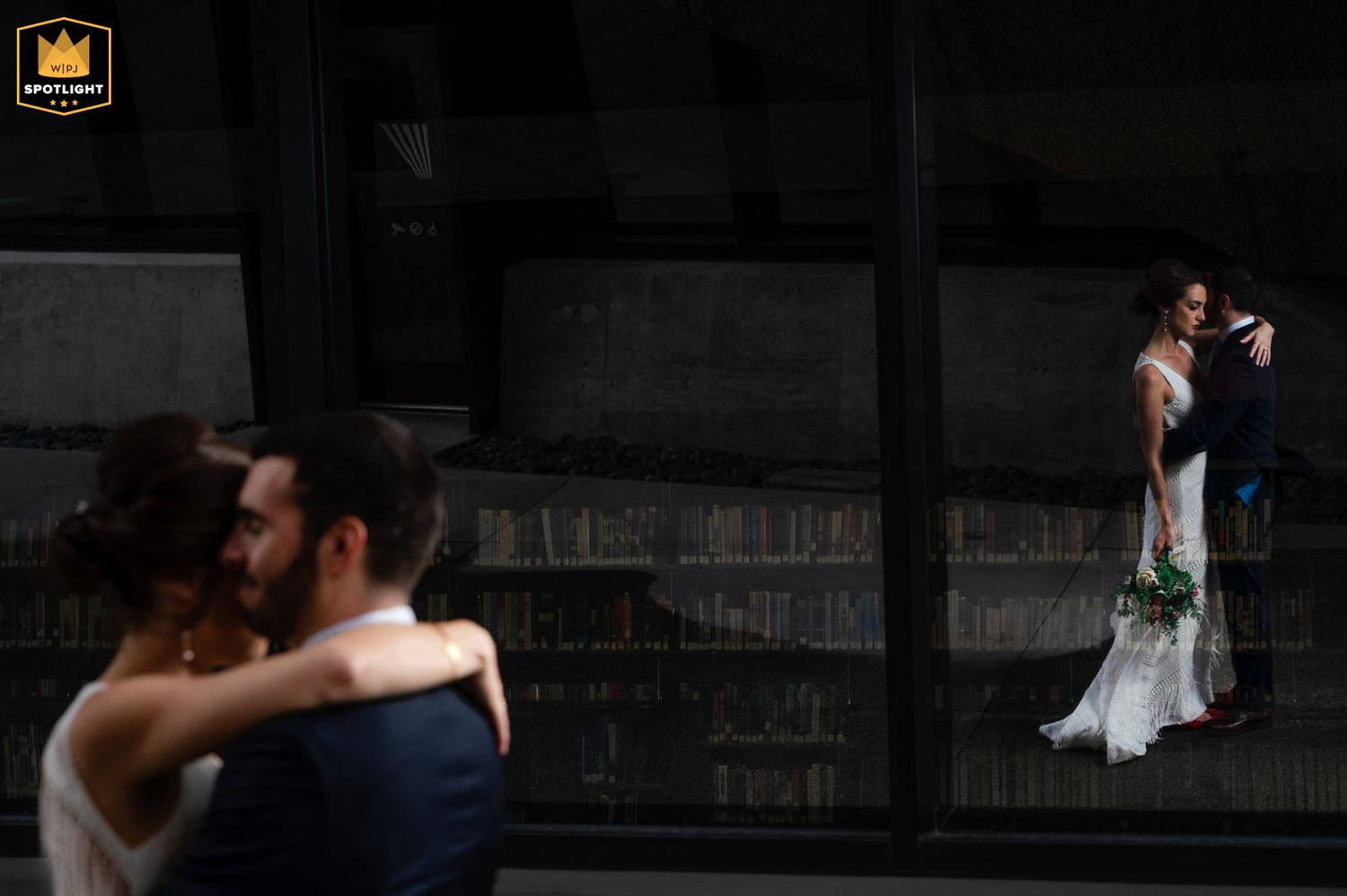 A couple embraces in the foreground while another stands in dramatic lighting against a dark urban wall in the background.