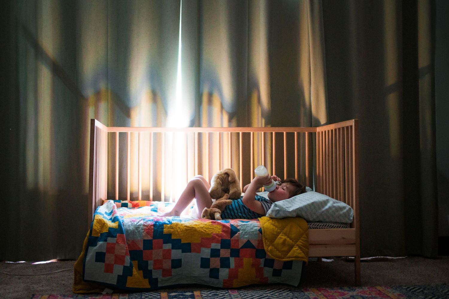 Dark interior view of a baby crib with colorful blankets and toys.