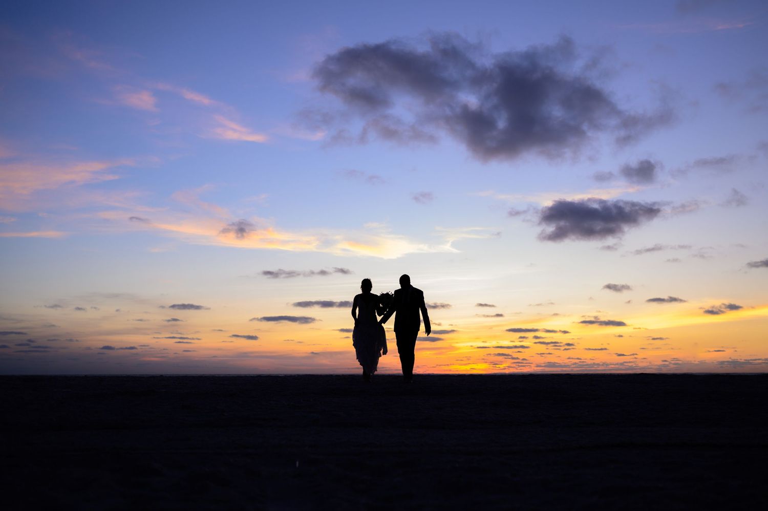 Two silhouettes holding hands against a vibrant sunset sky.