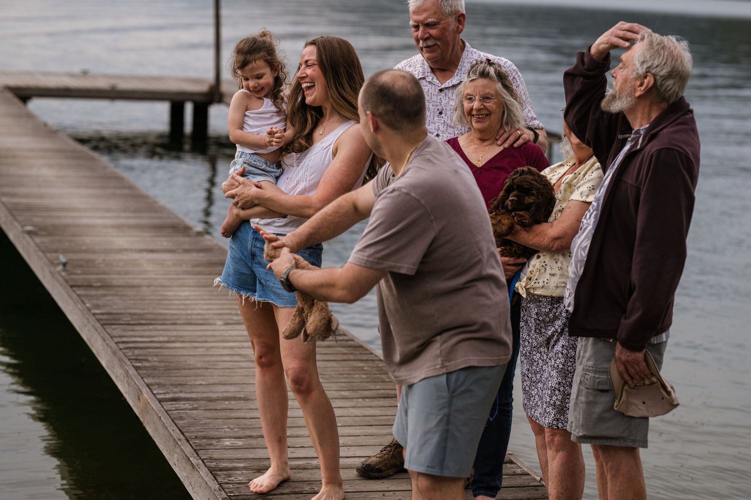 Multi-generational family gathering together on a wooden lake dock at dusk.