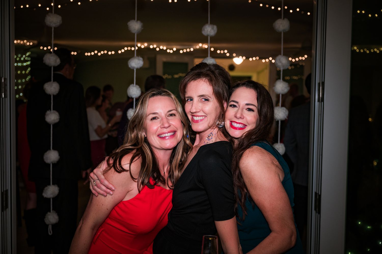 Friends pose together at an evening celebration with string lights in the background.