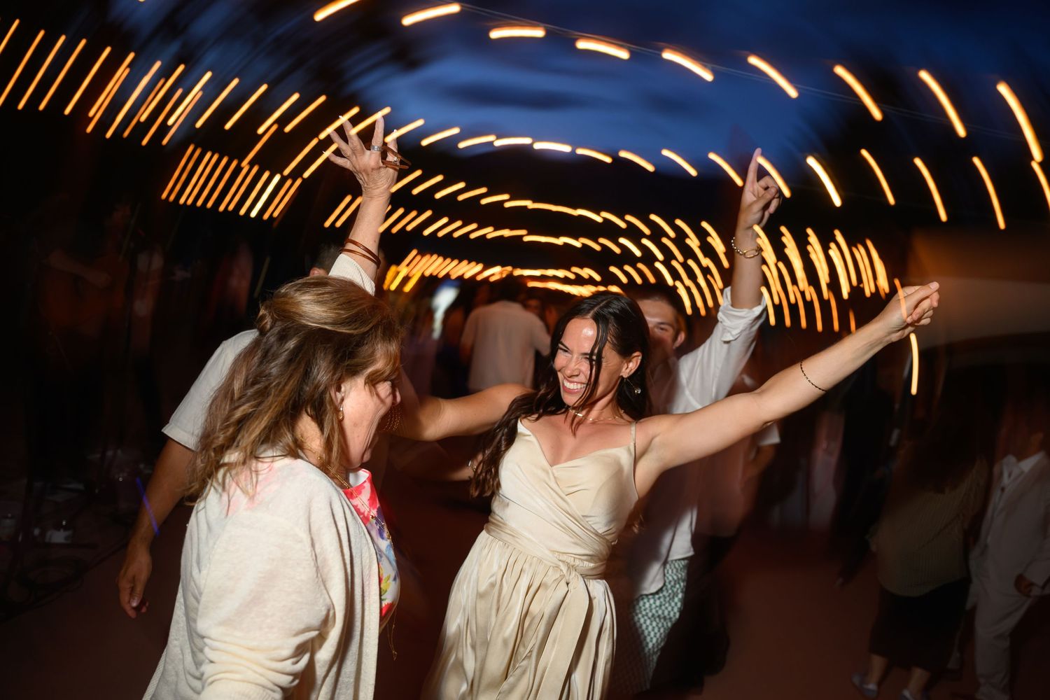 Wedding guests dancing and celebrating under glowing string lights at an evening reception.