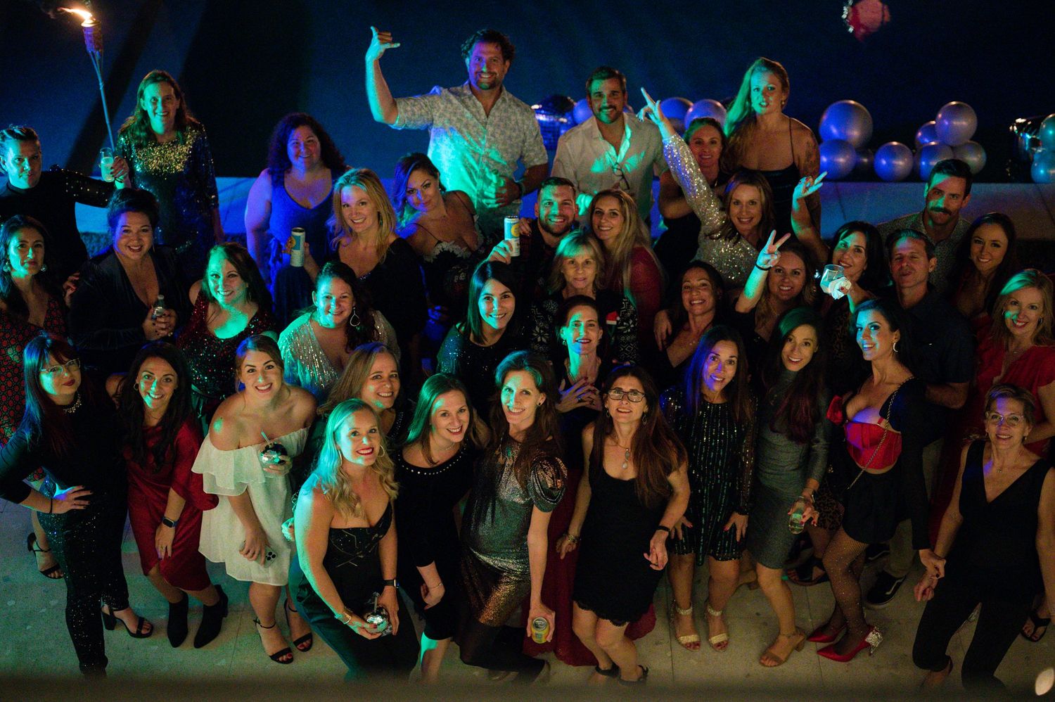 Large group photo of party attendees illuminated by colorful stage lighting.