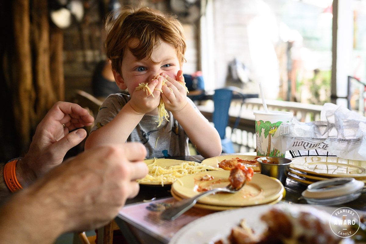Young child eating pancakes at a restaurant table with an adult, enjoying a casual breakfast meal.