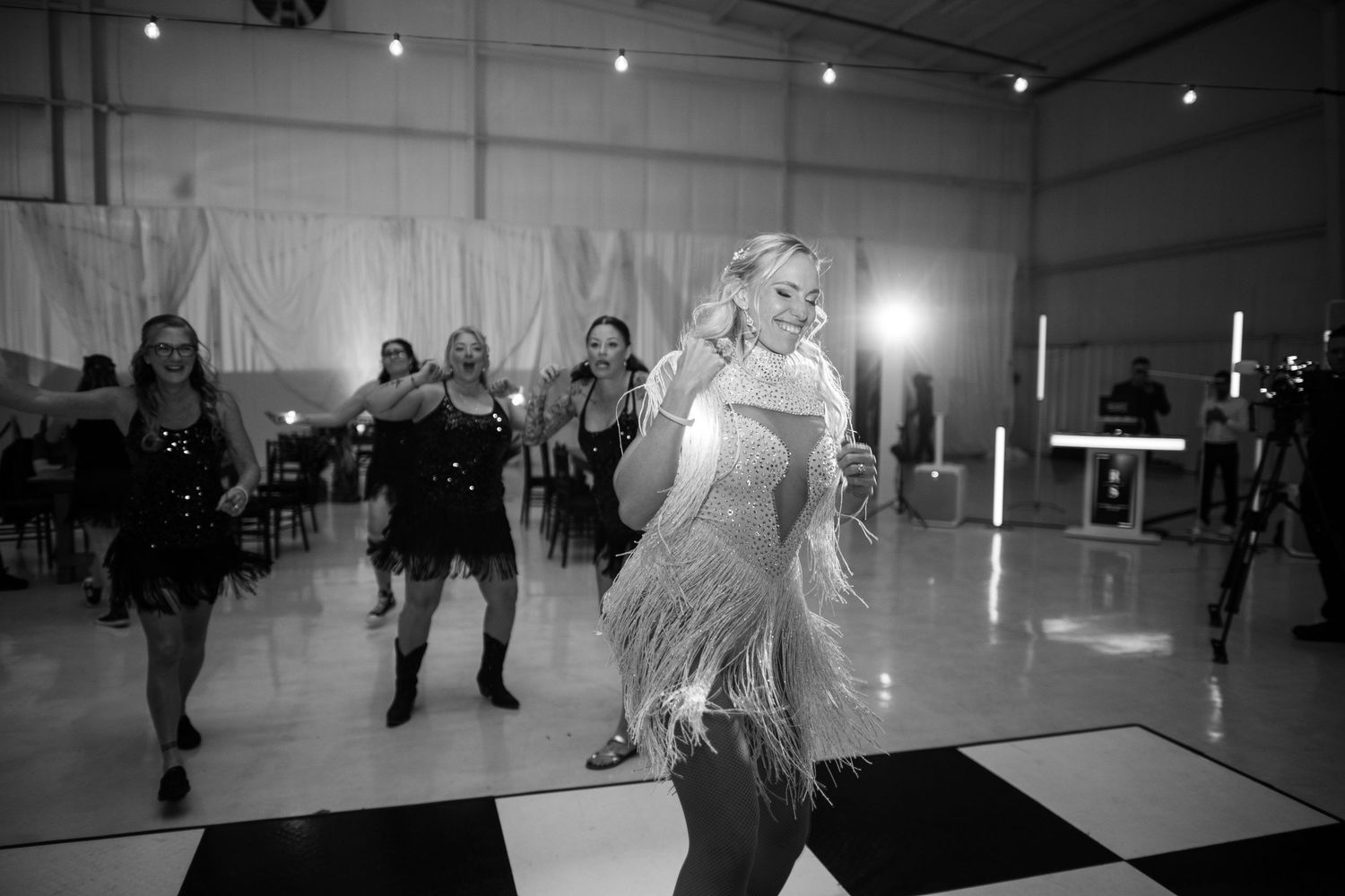 Black and white photo of women in fringe dresses dancing on a checkered dance floor at an elegant event.