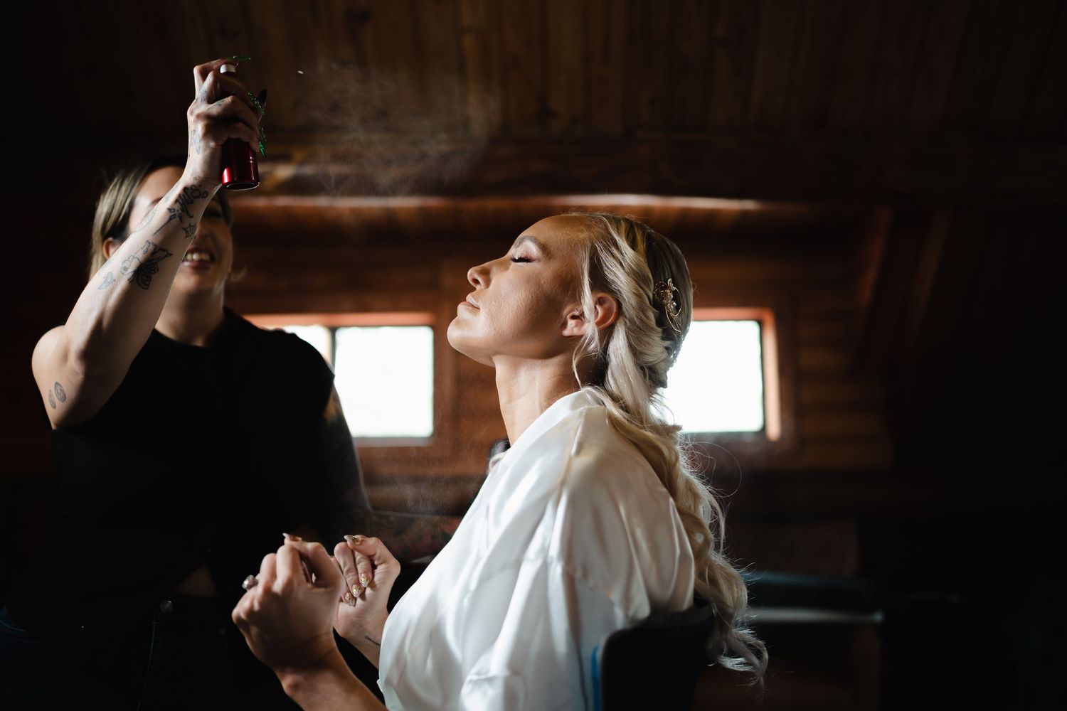 Bride getting hair and makeup done in rustic wooden cabin before wedding ceremony.