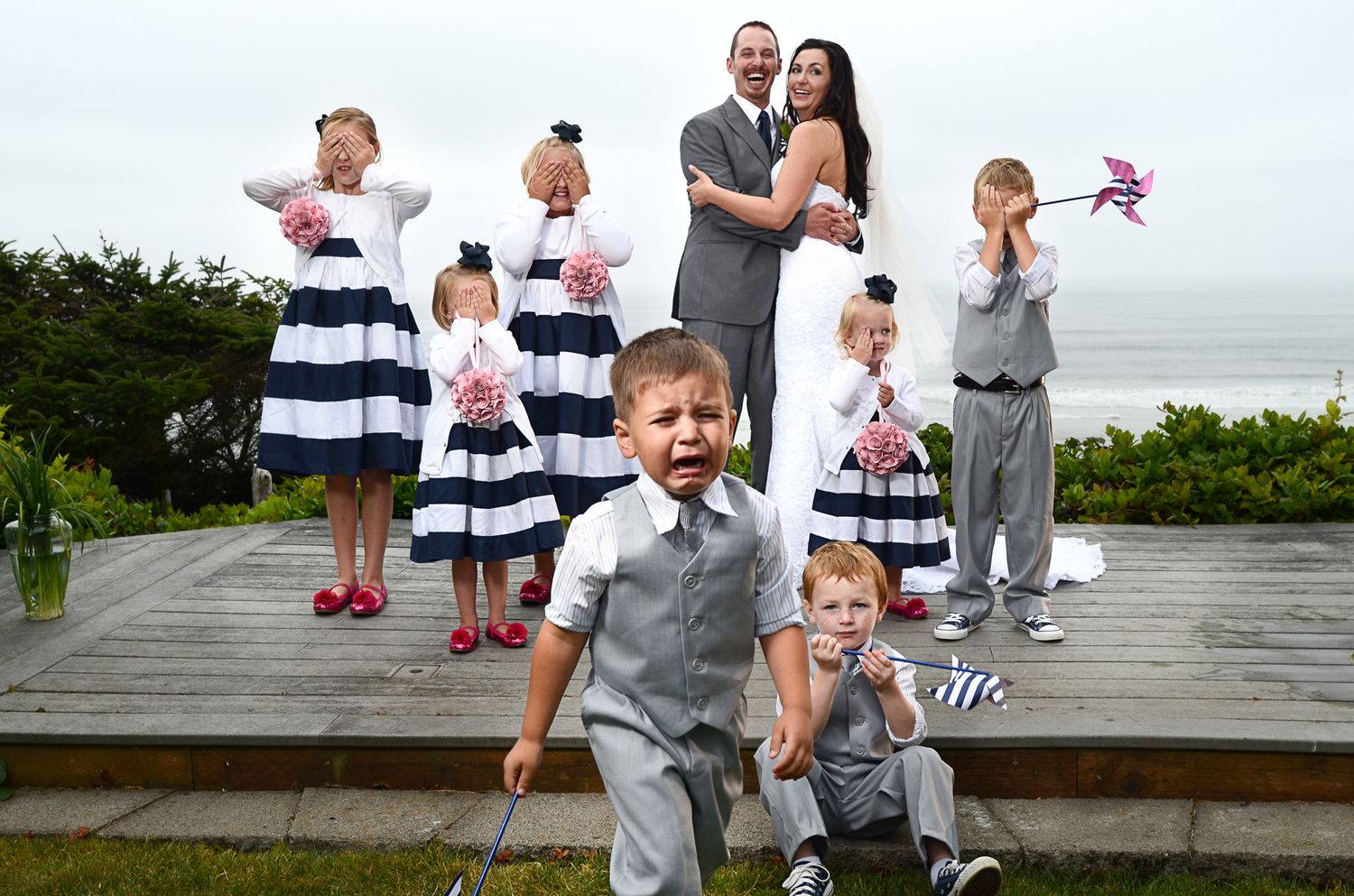 Wedding party members in coordinated outfits enjoying a playful moment on a seaside boardwalk.