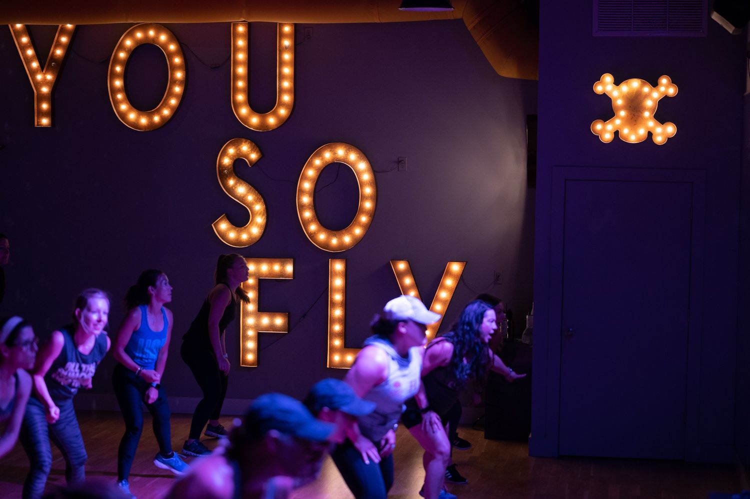 Energetic dancers performing under illuminated 'YOU SO FLY' marquee letters.