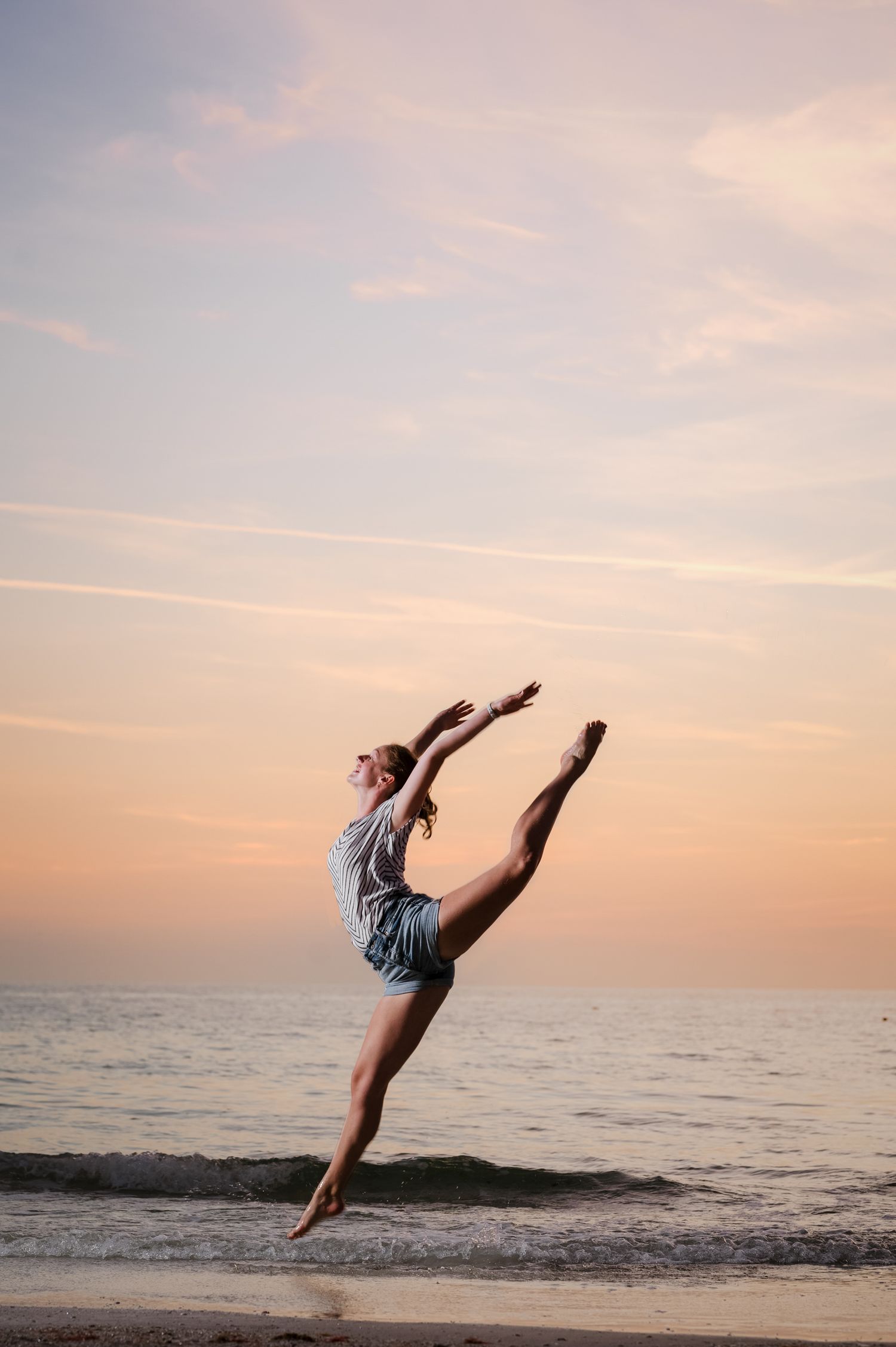 A dancer performs graceful leaps and poses on a beach at sunset, creating a beautiful silhouette against the pink sky.