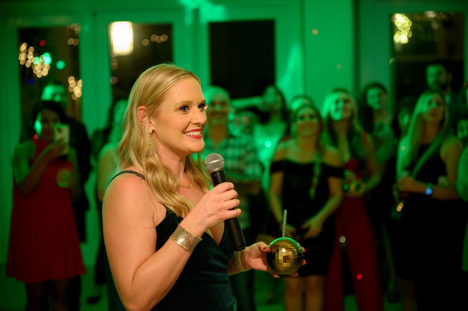 Party guest speaks into microphone under green lighting during festive celebration.