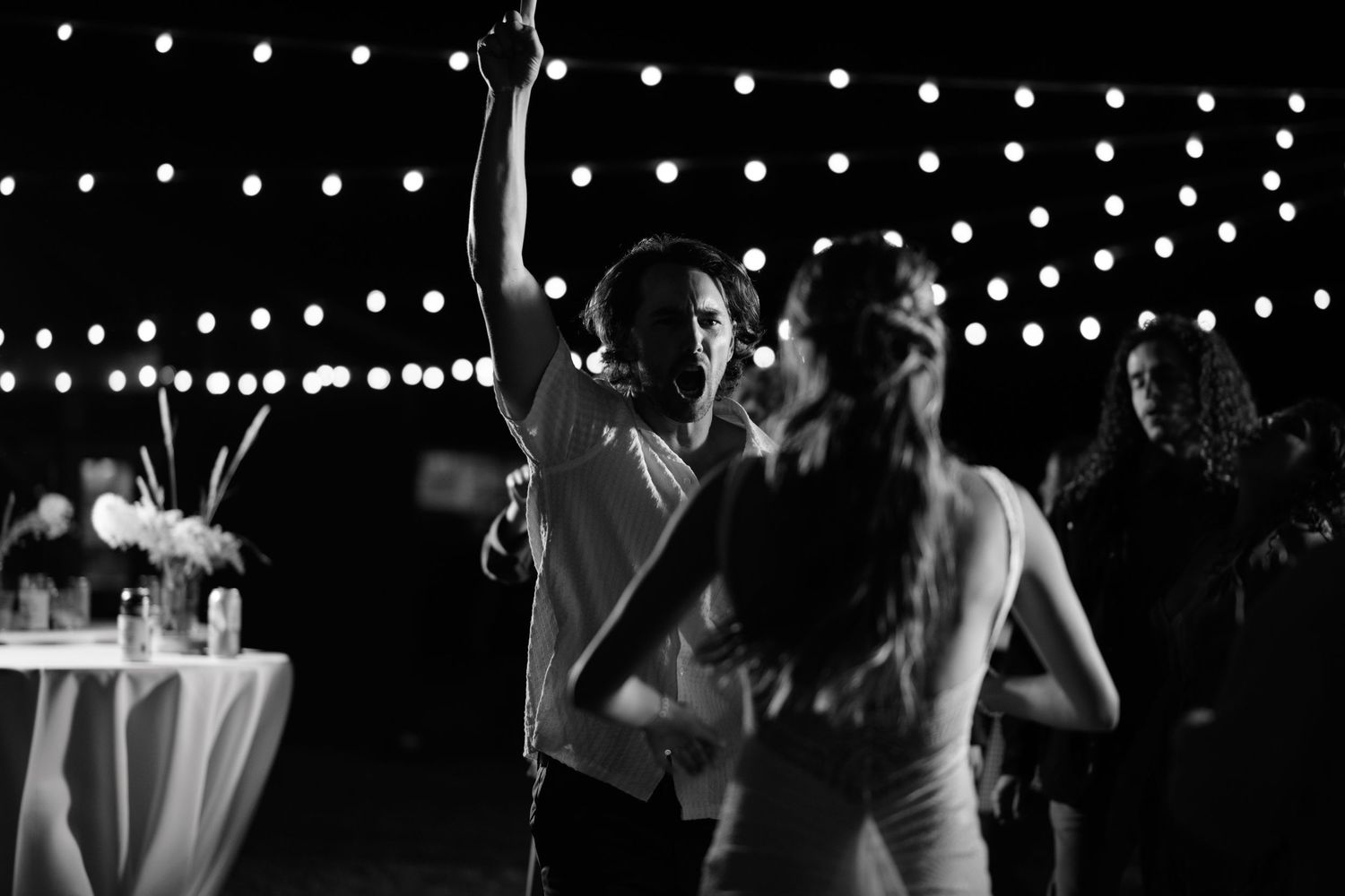 String lights illuminate a dark dance floor while people dance and celebrate at an evening event.