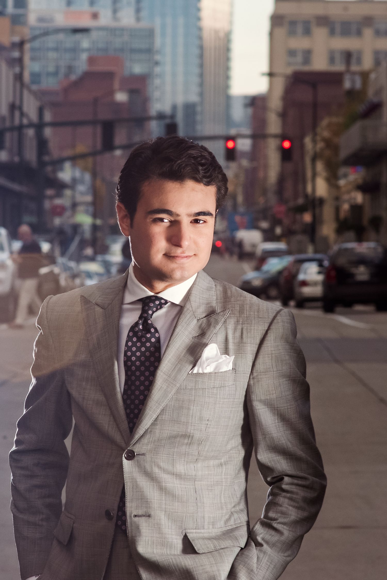 Professional headshots of someone in a grey suit and polka dot tie against an urban background.
