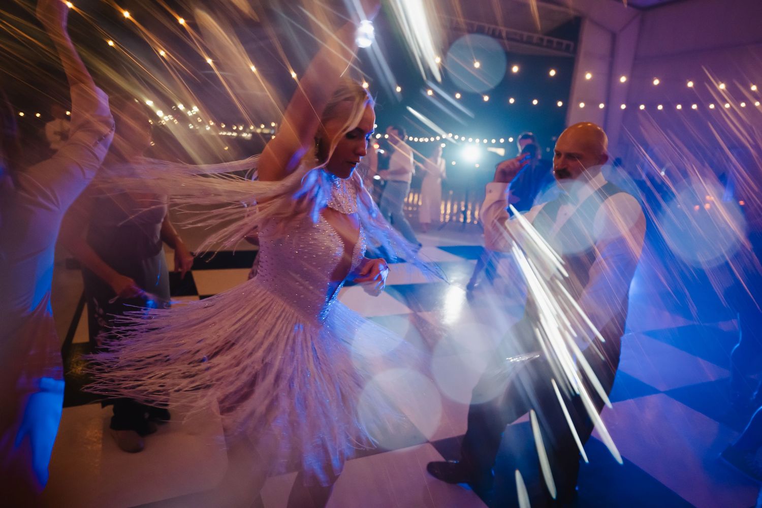 Bride and guests dancing energetically on a wedding reception dance floor with sparkling lights and blue ambient lighting.