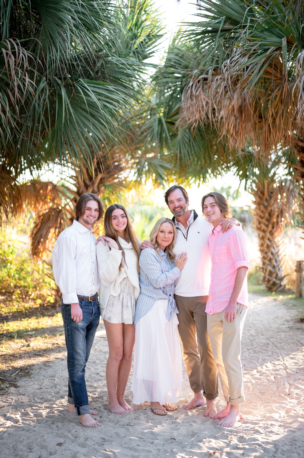 A group stands together outdoors in casual attire with palm trees visible in the background during golden hour.