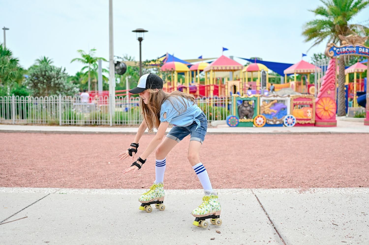 Kids skateboarding at a colorful playground with palm trees and blue canopies.