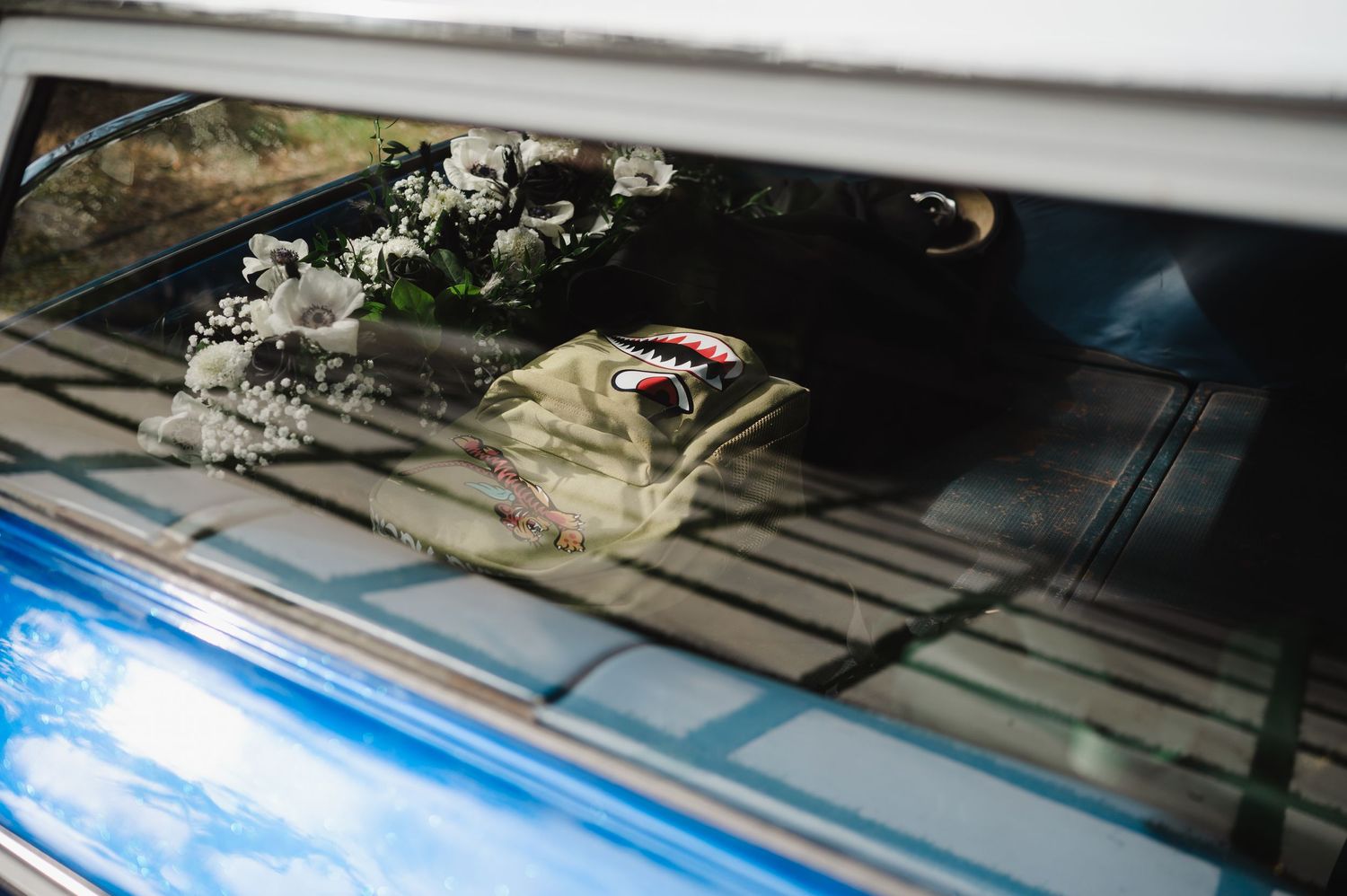 Wedding bouquet and accessories visible through blue vintage car rear window.