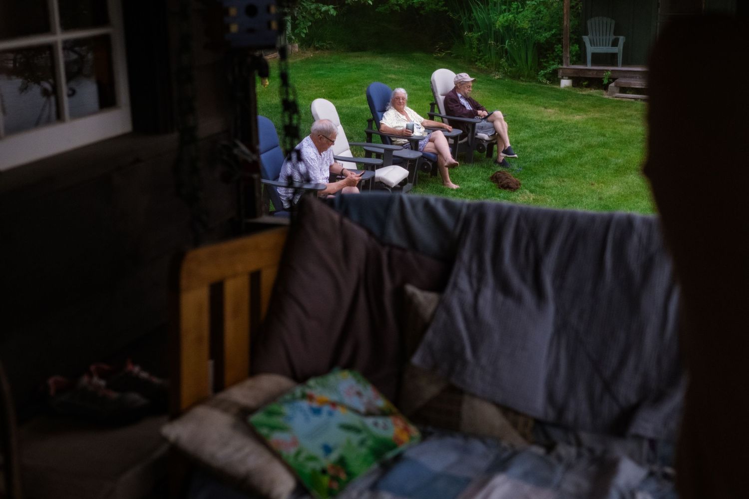 Elderly women relaxing outdoors in garden chairs, viewed through a window with blankets in foreground.