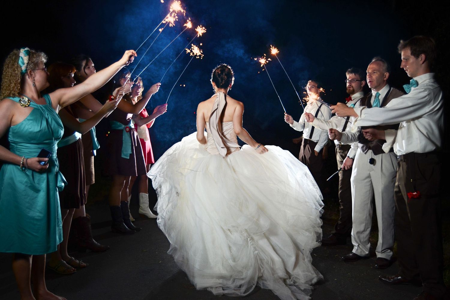 Wedding party sparkler exit at night with guests creating a glowing tunnel for the newlyweds.