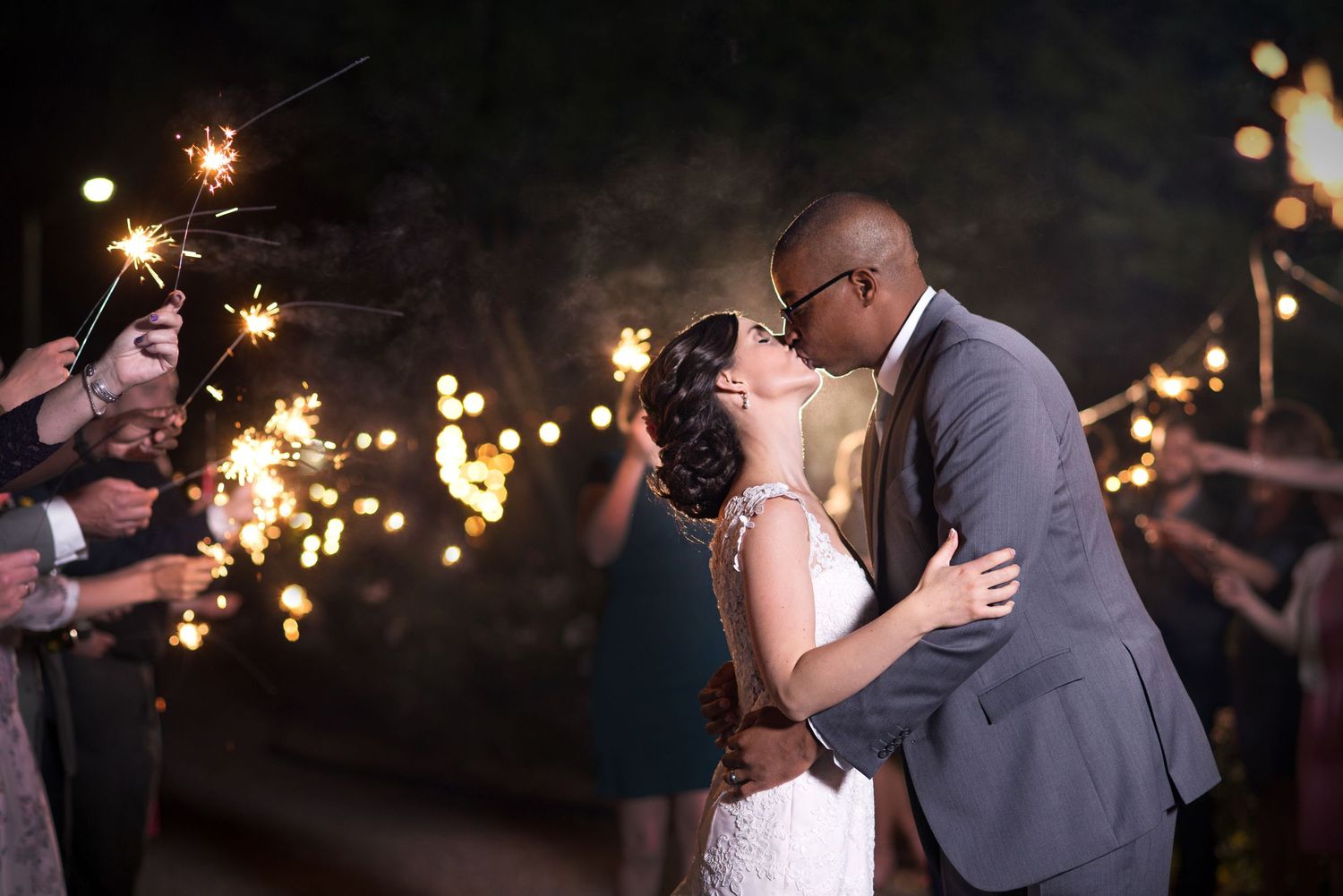 Couples slow dancing beneath warm string lights at an intimate evening reception.