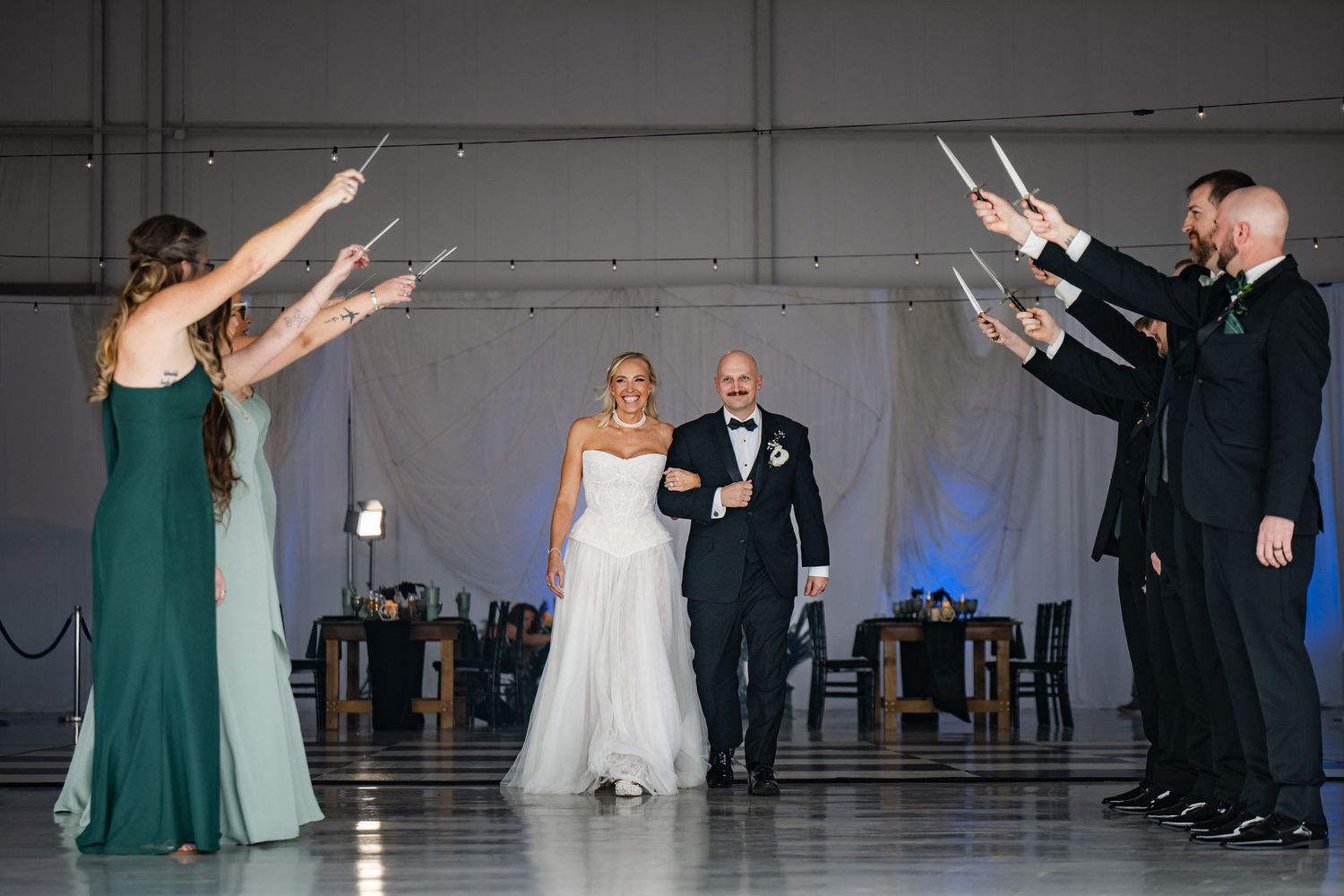 Bride and groom walk through a sparkler tunnel during their wedding reception in an elegant hangar venue.