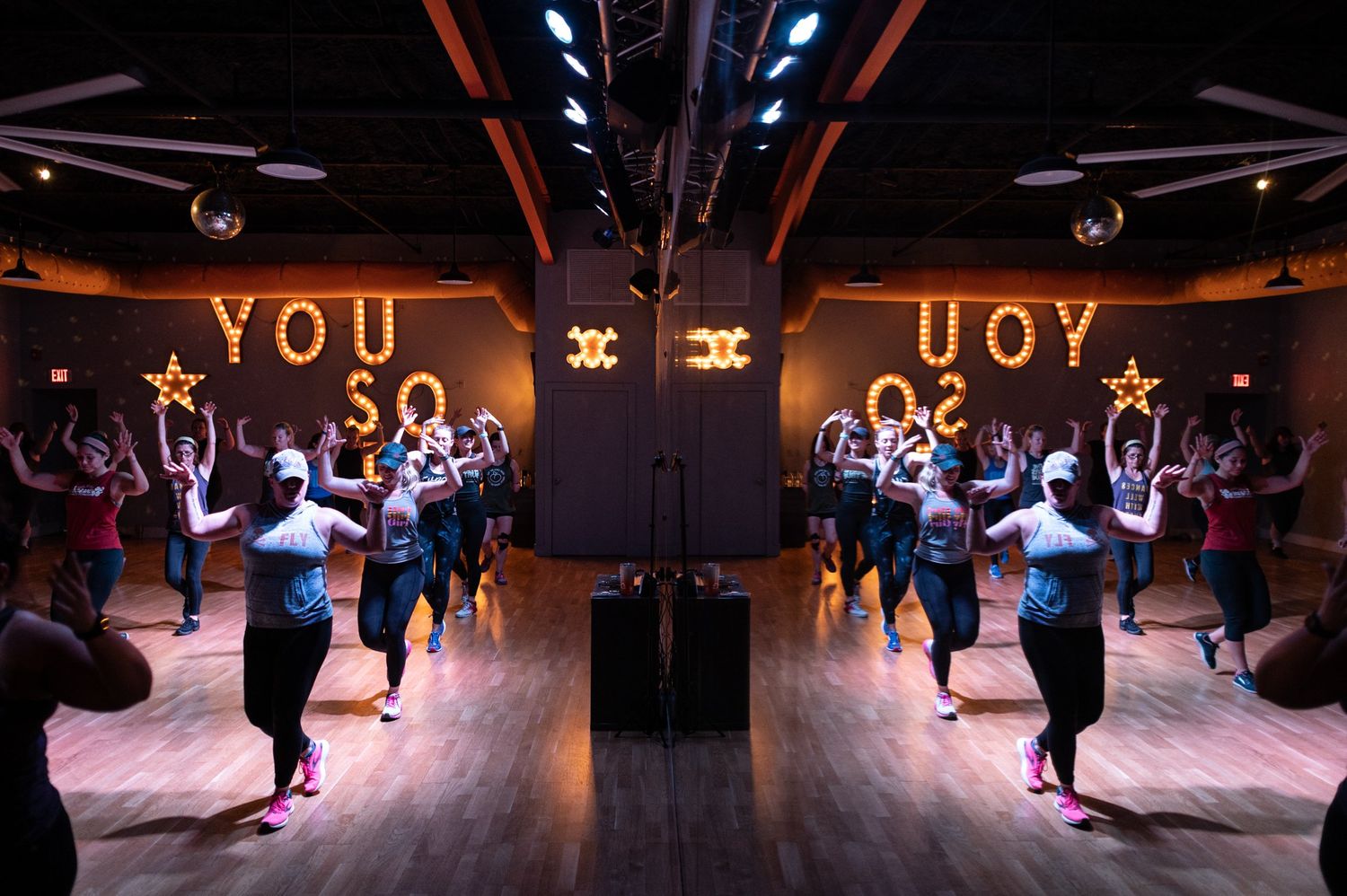 Dance class participants practicing choreography in a mirrored studio with neon lighting.