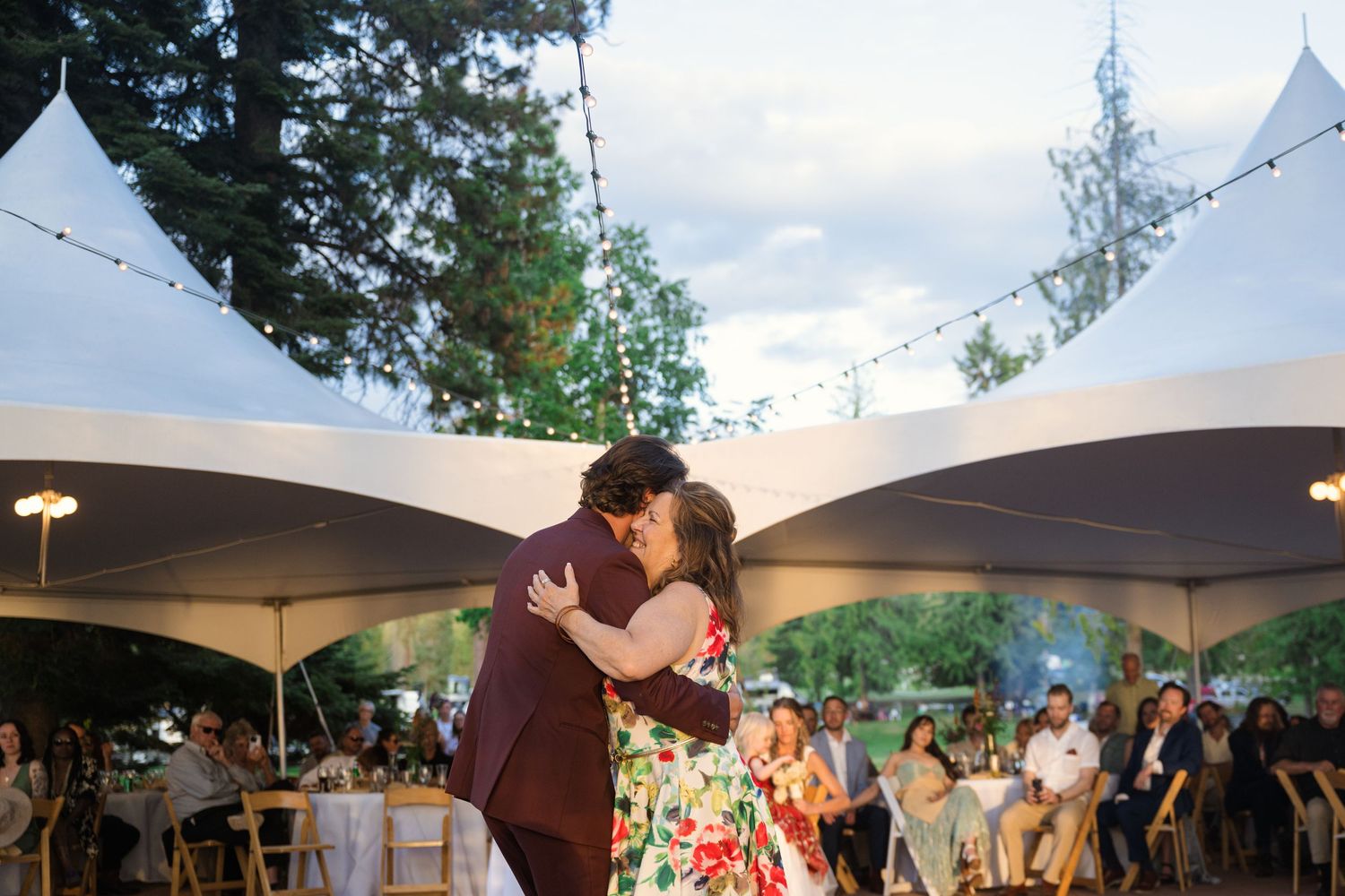 Couple shares an intimate dance under white tent canopies at an outdoor reception with guests in the background.