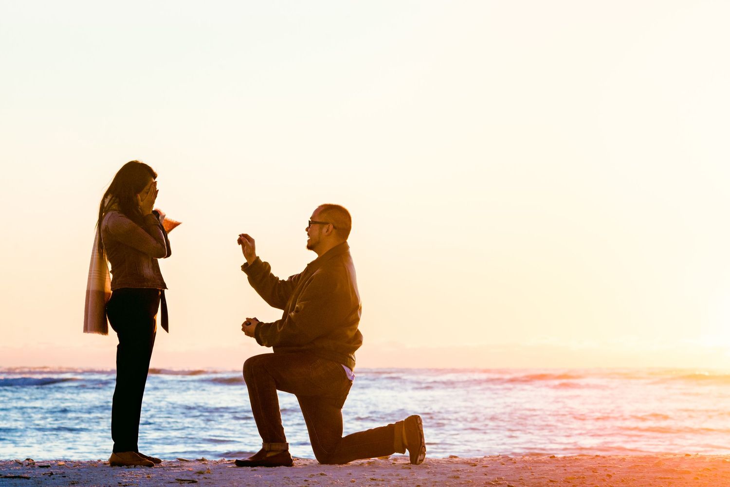 Silhouette of a proposal on the beach at sunset with waves crashing in the background.