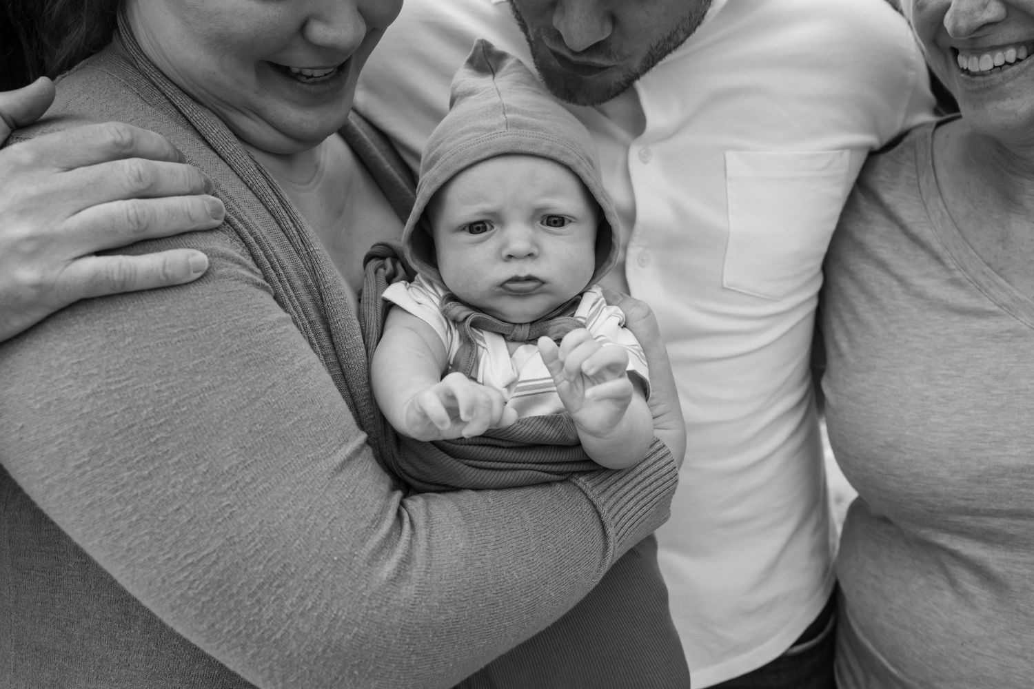Black and white photo of two adults holding a newborn baby in a knit hat, family portrait.