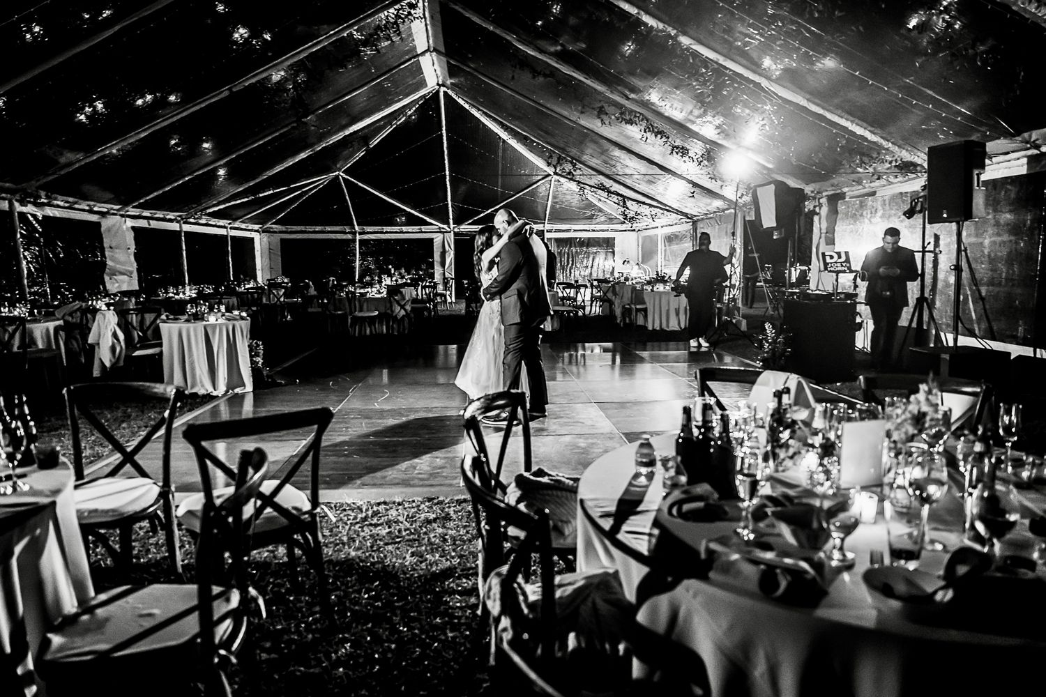 A black and white photo of a clear tent wedding reception venue with elegant table settings and ambient lighting.