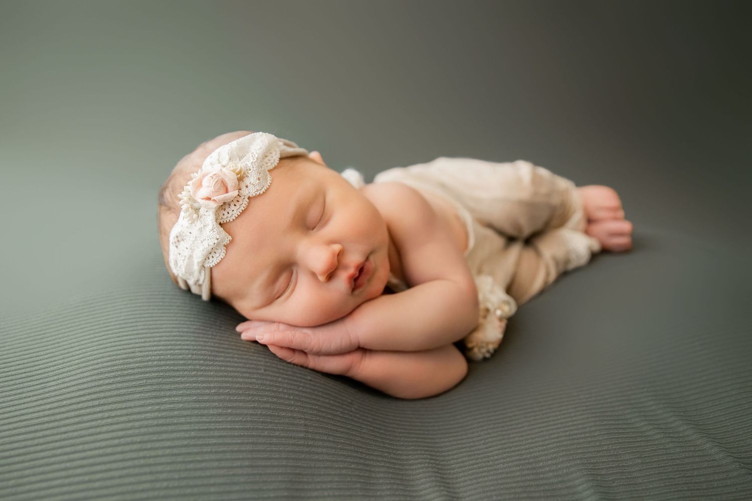 A sleeping newborn baby in a white onesie lies on a textured gray background in a peaceful pose.