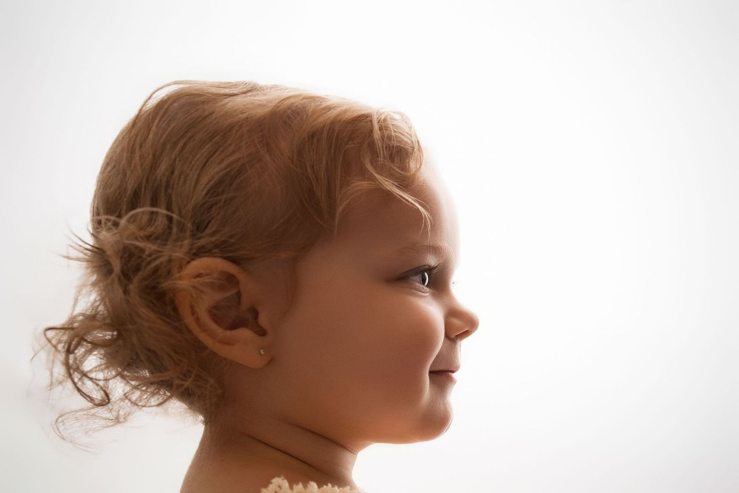 Side profile of a smiling toddler with curly reddish-brown hair against a white background.