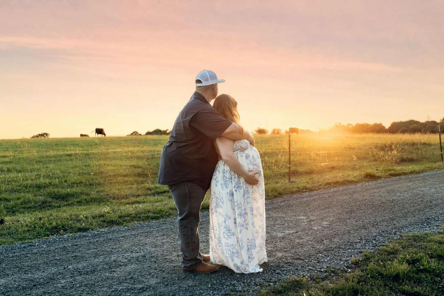 Couple embracing at sunset on a farm path, woman in floral dress and man in suit, golden hour light.
