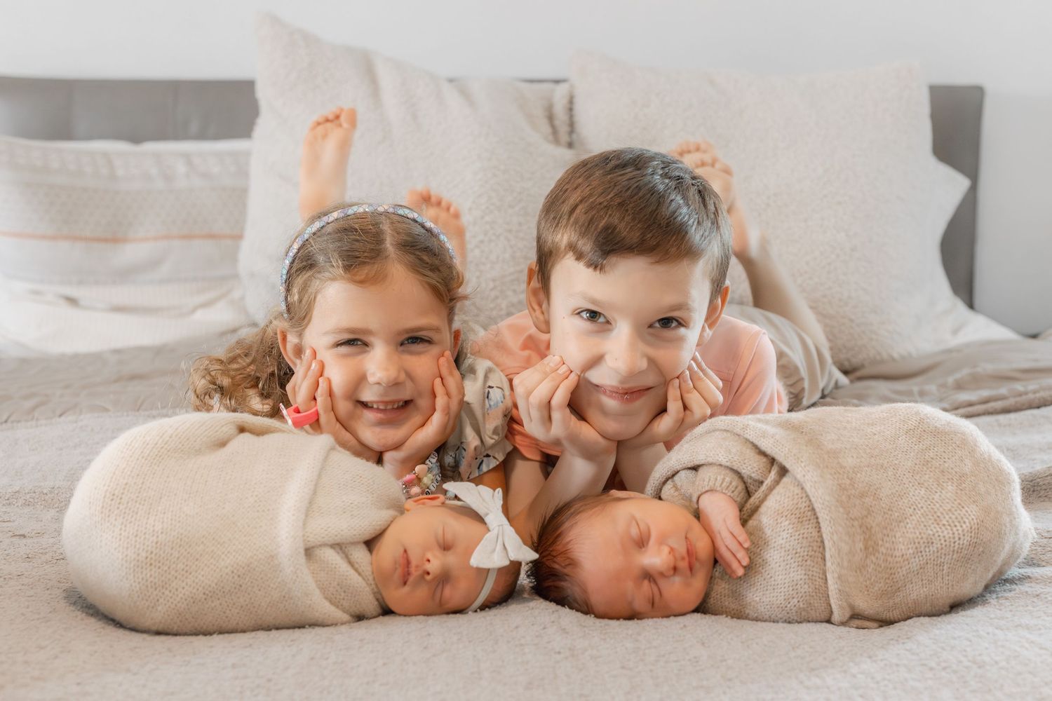 Happy children lying on a white bed in matching beige outfits smiling and playing together.