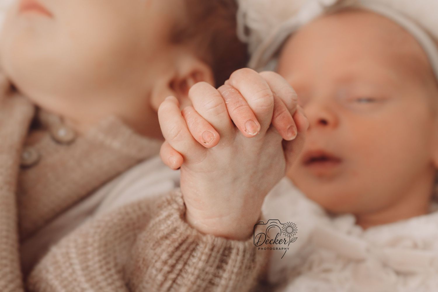 Close-up of tiny baby fingers grasping an adult hand against soft beige knitted fabric background.