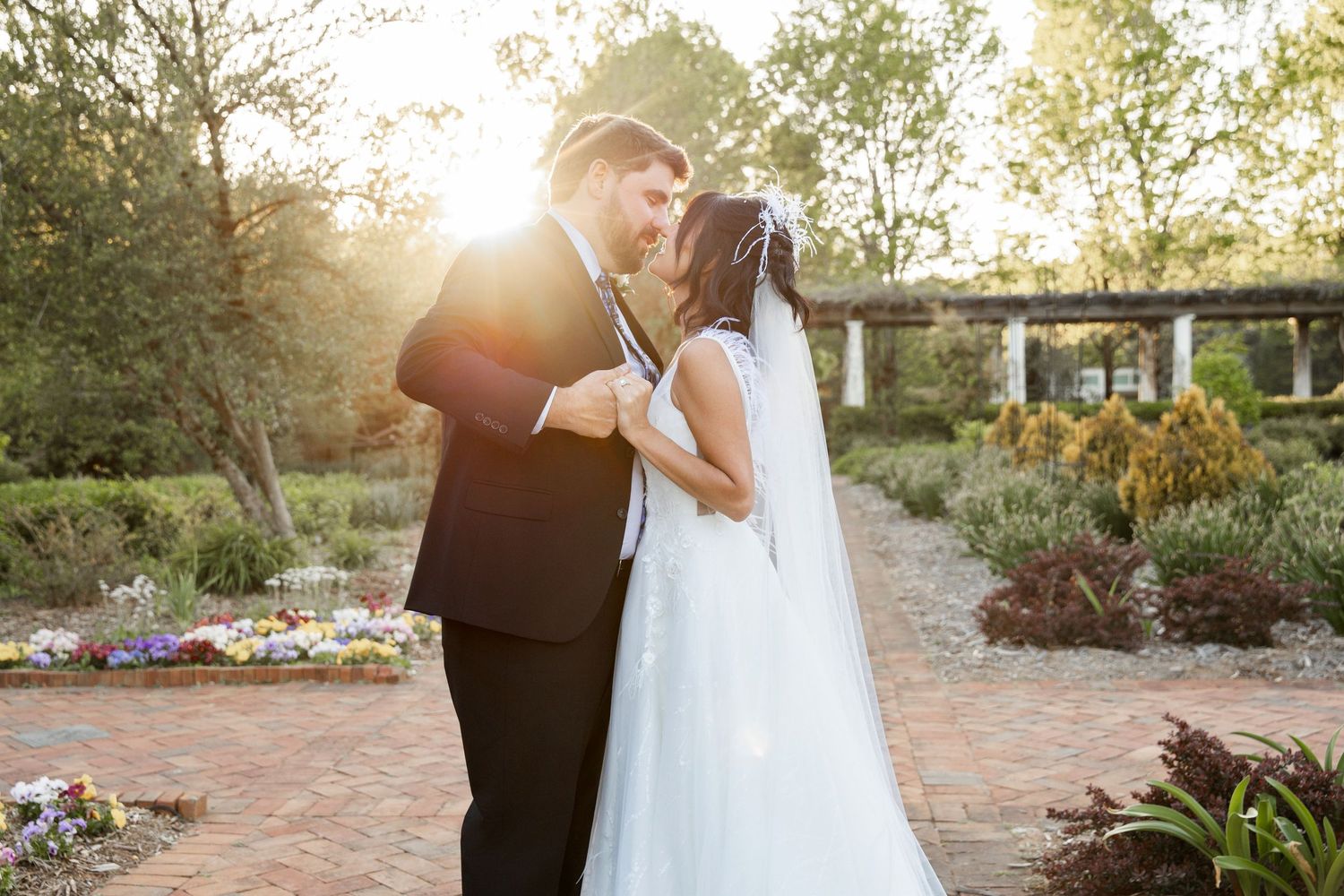 Bride and groom sharing a romantic kiss in a sunlit garden, bride wearing a white gown and veil.