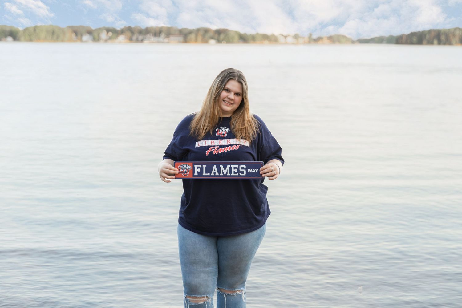 Young woman standing in water holding a Flames banner sign, wearing a navy blue t-shirt and jeans.
