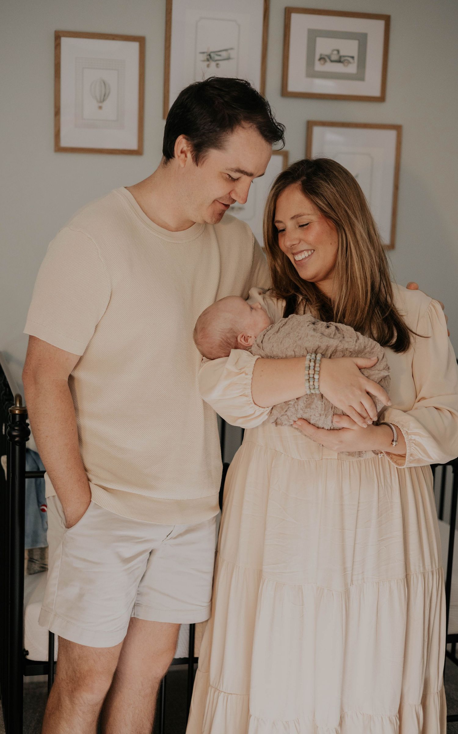 Happy couple in neutral tones smiling at newborn baby in softly decorated nursery room.