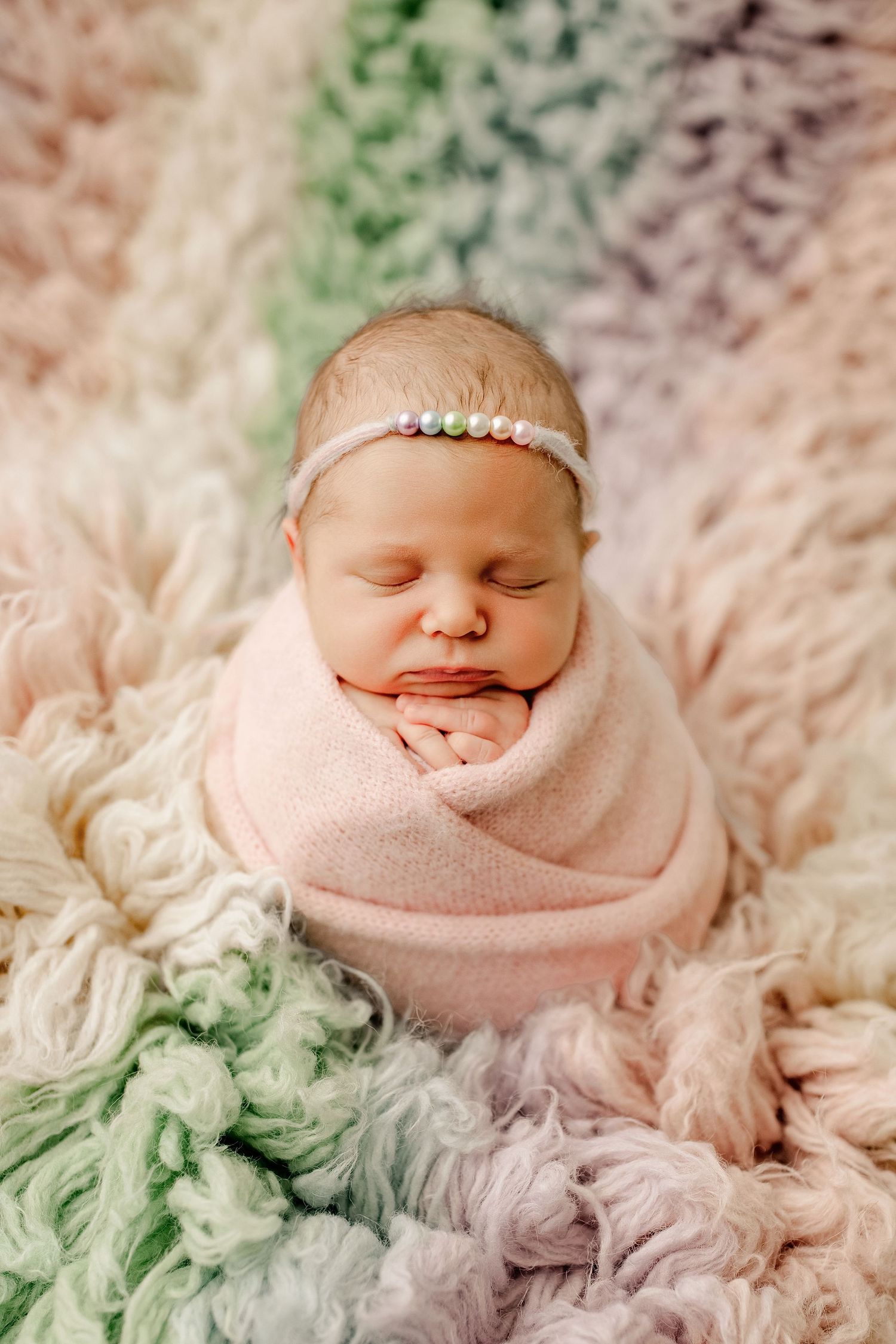 Newborn baby peacefully sleeping while swaddled in soft pink wrap on textured mint and cream colored blanket.