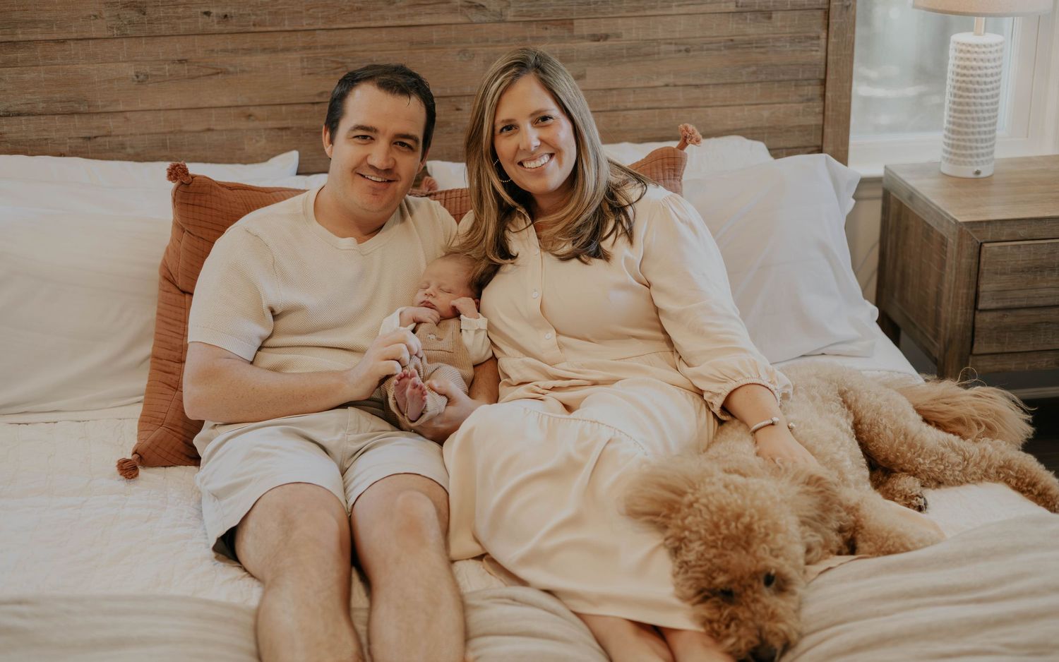 People lounging together on a cozy bed with wooden headboard and neutral decor in a warm, intimate setting.